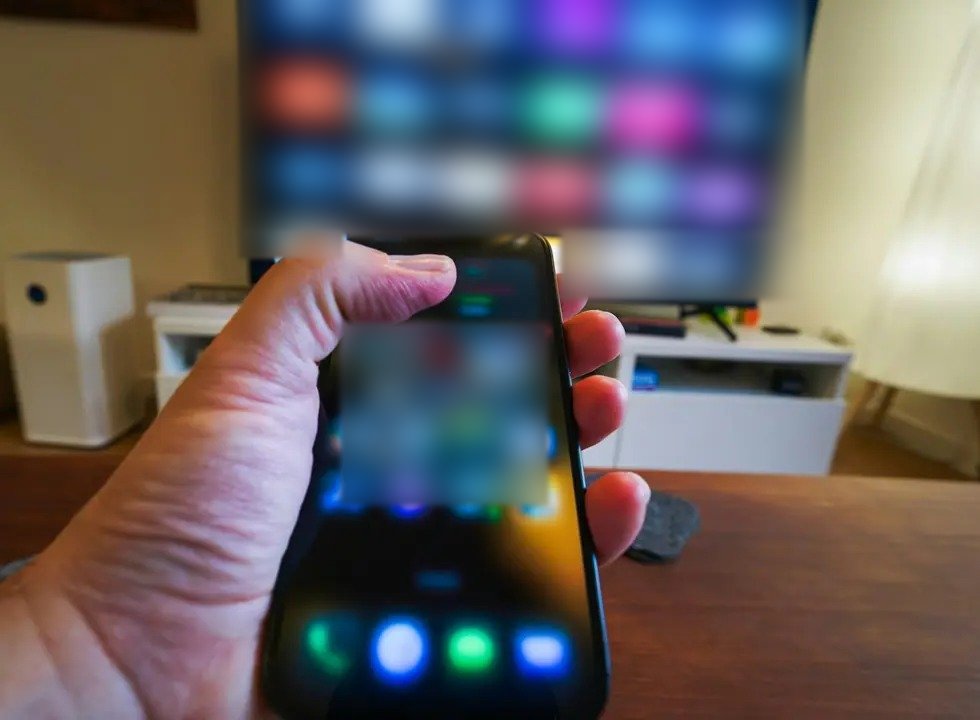 Elde telefon, arkada uygulama ekranı açık televizyon